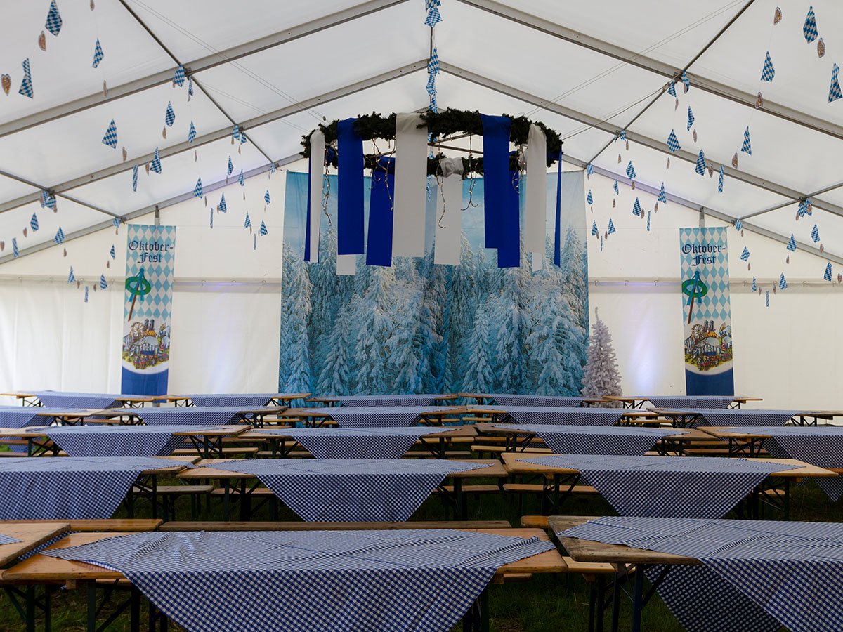 Bordene er dekoreret med blå og hvidternede duge. I loftet hænger en krans og bagved et banner med oktoberfest 