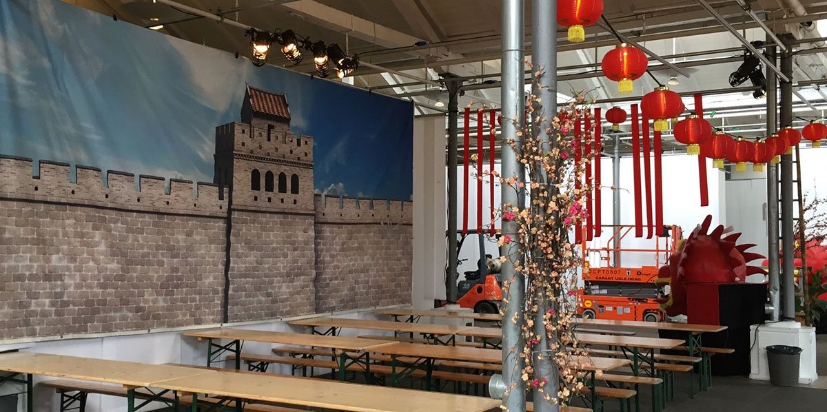 På væggen hænger et stort banner med et billede af den kinesiske mur og i loftet hænger kinesiske lamper 
