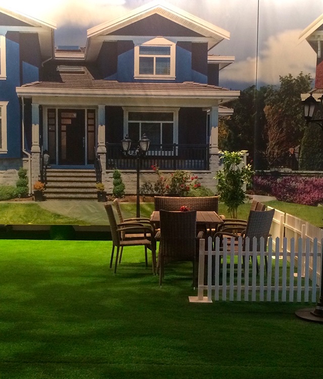 En havefest er dekoreret med græs, havemøbler, blomster, stakit og et stort banner med et billede af en villavej 