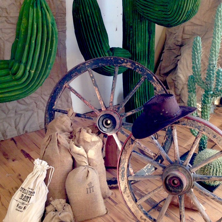 Billede af gamle træhjul, kaktusser, sandsække og en cowboyhat 