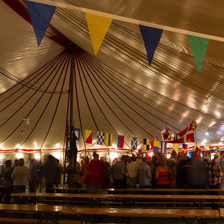 Her holdes sømandsfesten i et telt. hvor der hænger flag i teltdugen 