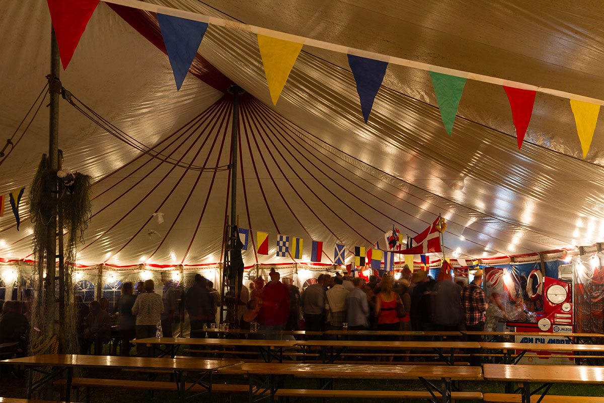 Her holdes sømandsfesten i et telt. hvor der hænger flag i teltdugen 