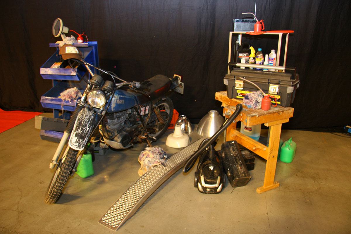 En gammel motorcykel står omringet af ting fra et bilværksted 