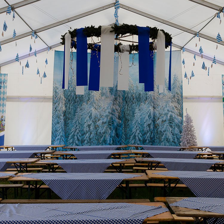 Bordene er dekoreret med blå og hvidternede duge. I loftet hænger en krans og bagved et banner med oktoberfest 