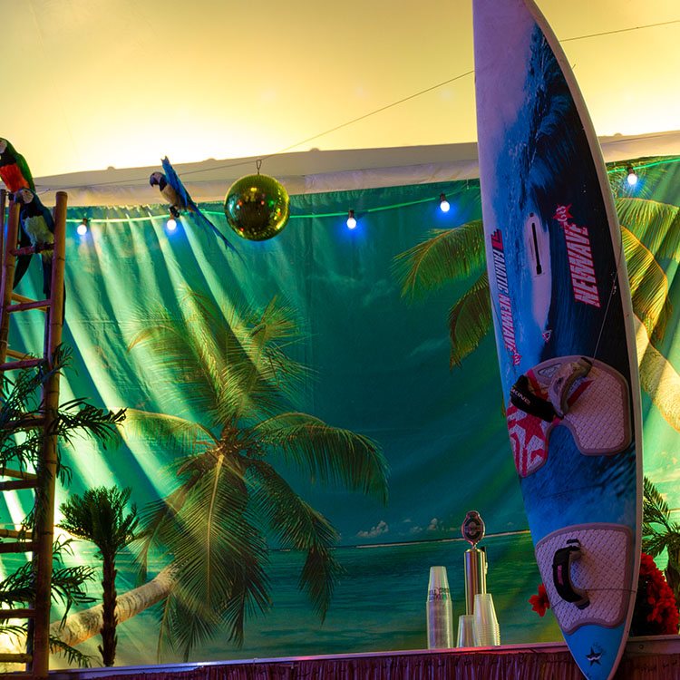 Baren er pyntet med et banner med et billede af en tropisk strand, et surfboard og papegøjer 