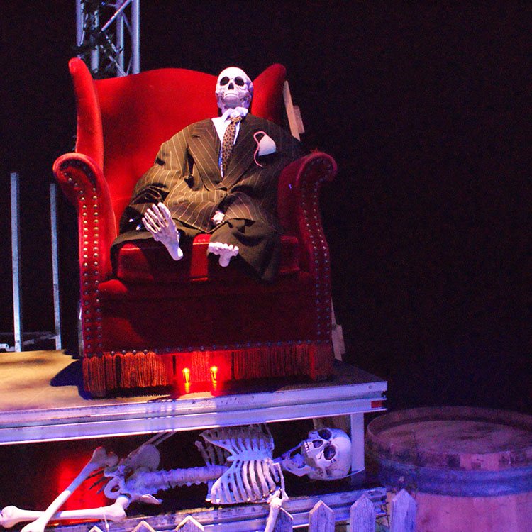 På scenen sidder skelettet af en mand i en rød stol. Under scenen ligger endnu et skelet og kigger ud på gæsterne 