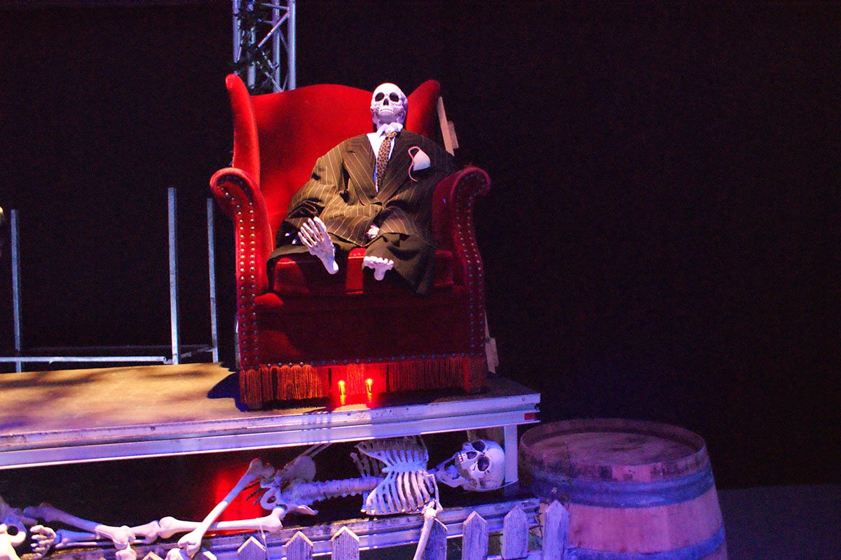 På scenen sidder skelettet af en mand i en rød stol. Under scenen ligger endnu et skelet og kigger ud på gæsterne 