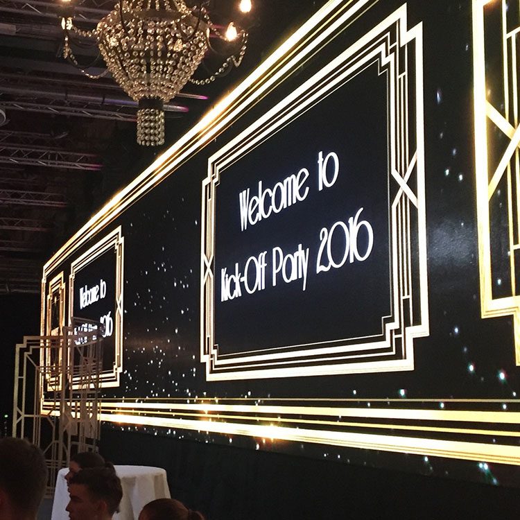 På væggen hænger et stort banner i sort og guld, som byder gæsterne velkommen til Gatsby festen 