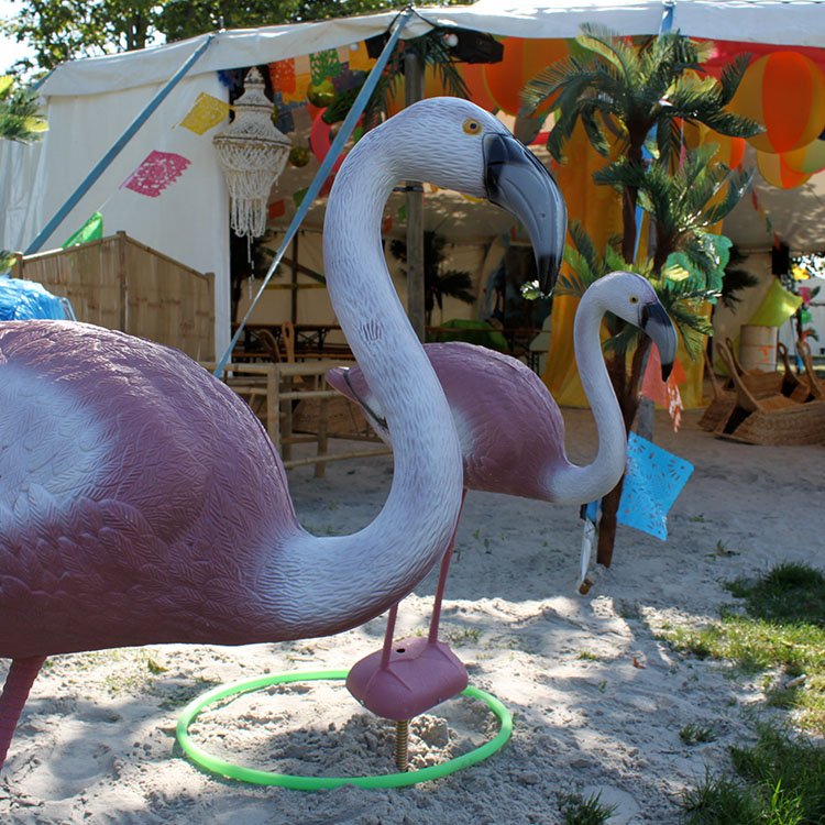 Store plastik flamingoer står i sandet 