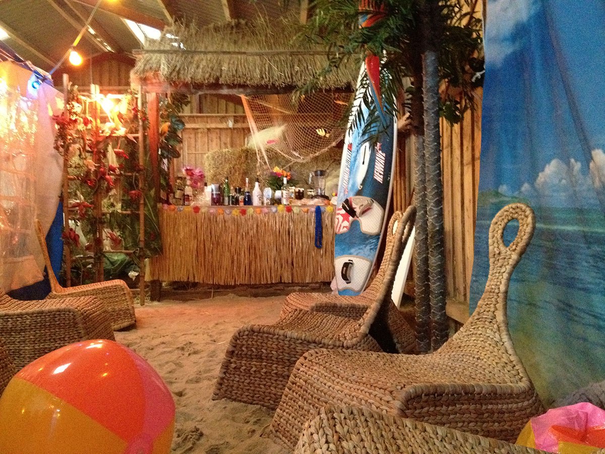 Denne beach party er pyntet med sand, strandmøbler, et surfboard, en træbar, blomster og badebolde